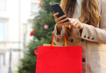 Was Österreicher zu Weihnachten schenken Shopper woman using smart phone for shopping online and carrying bags on Christmas time.